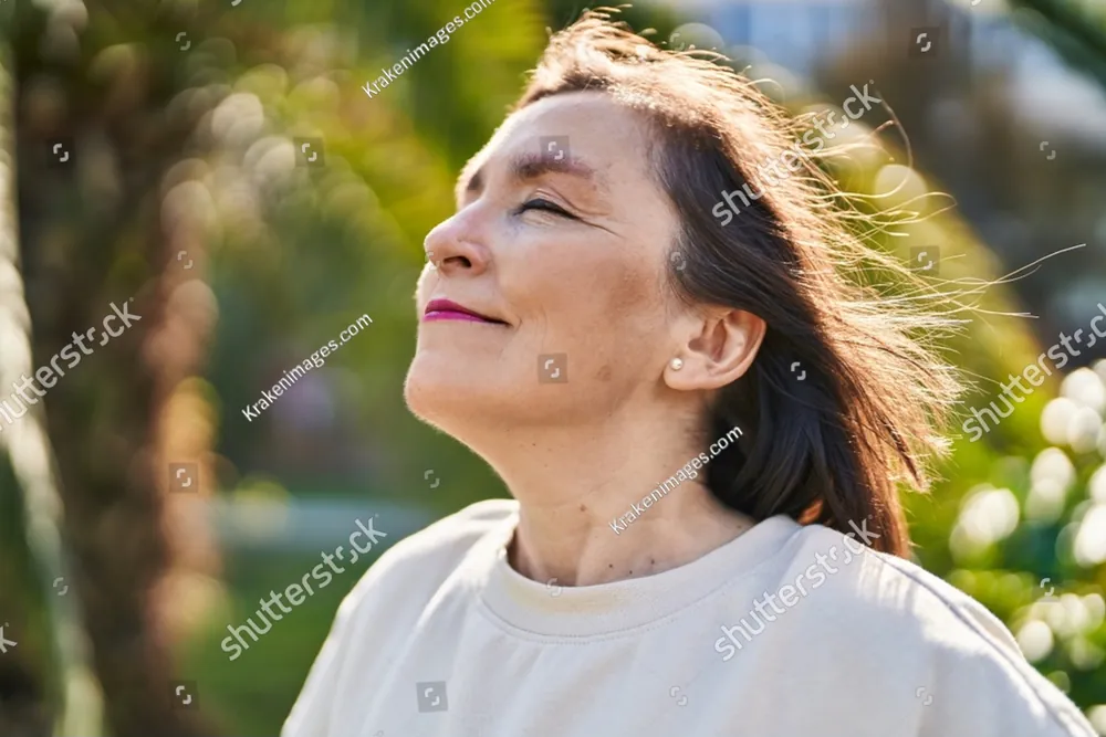 A woman with her eyes closed, her face lifted to the sun in a garden