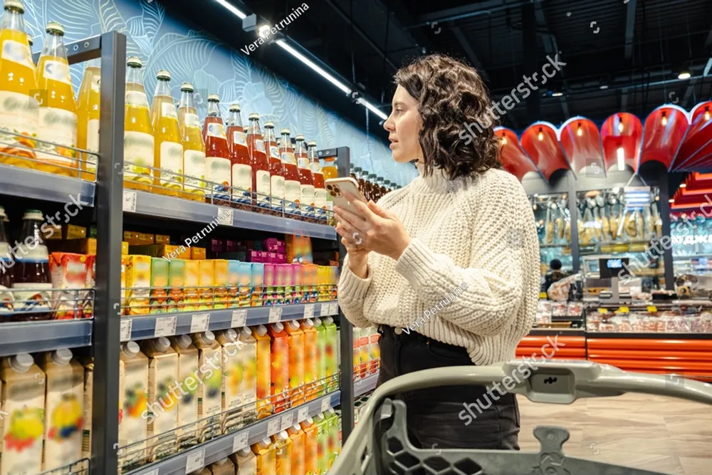 A woman in a cream sweater checking her phone in a grocery aisle