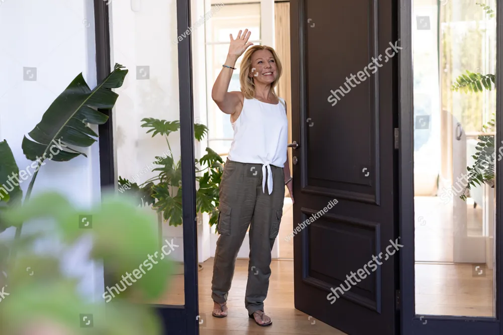 A smiling woman waving from her open front door
