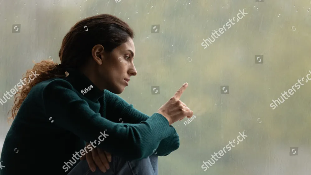 A woman sitting by a misty window, reaching toward the glass