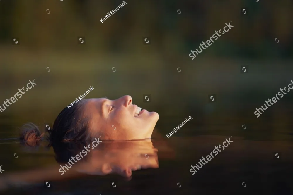 A woman floating on her back in calm water, her eyes closed